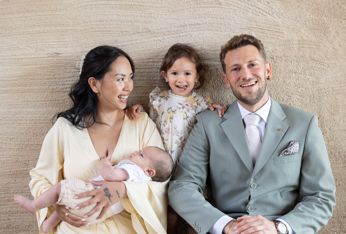 Familjeporträtt mot en sandfärgad vägg med bebis och litet barn