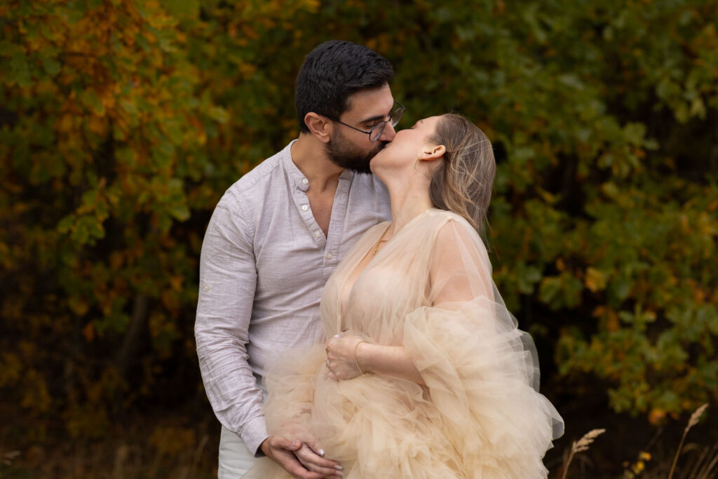 Gravidfotografering utomhus, gravida par kysser varandra